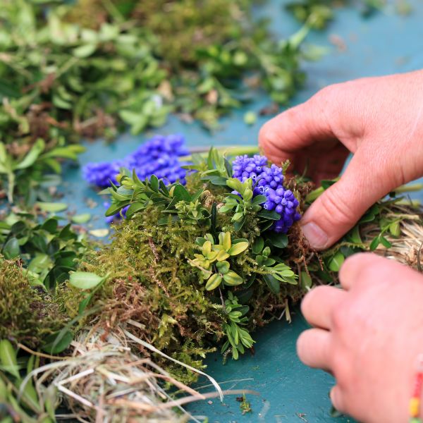 person putting moss and greenery on a wreath base