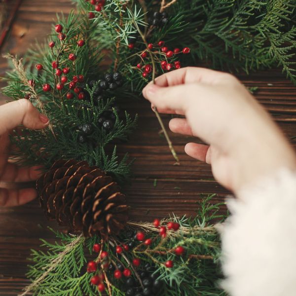 person adding pinecones and berries to a christmas wreath