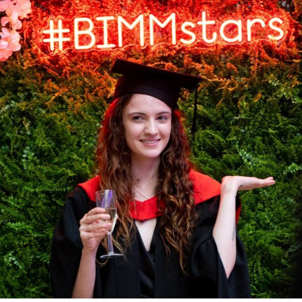 Graduate in front of a flower wall with a light up flower sign